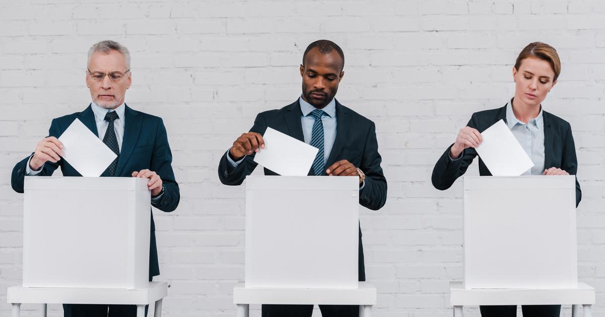 Zwei Männer und eine Frau stecken ihren Wahlzettel in die Urne. ©Envato